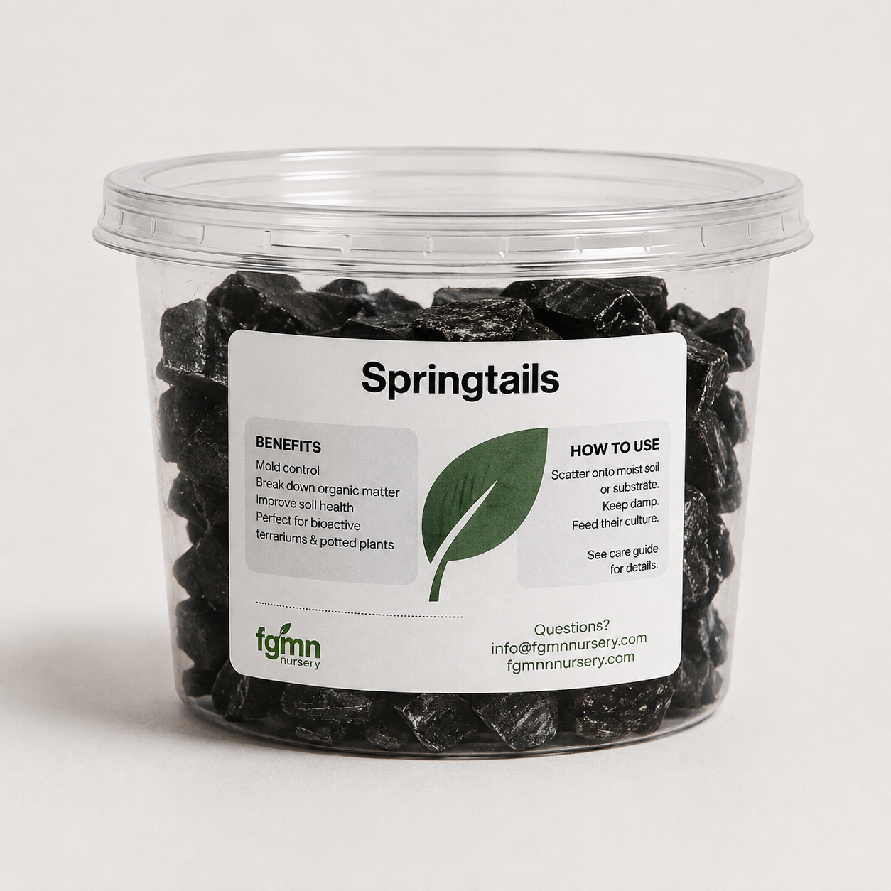 A clear plastic tub filled with dark, irregularly shaped organic moss control granules labeled 'Springtails' by fgmn nursery, on a light gray background.