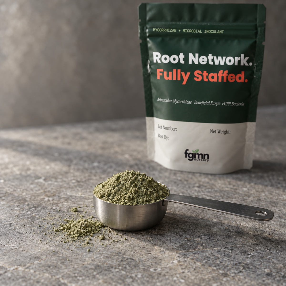 A steel scoop heaped with light olive-green Root Network powder on grey stone, with the dark green Root Network pouch standing behind it.